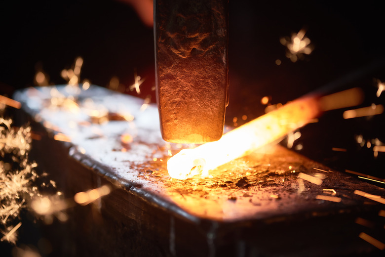 Close-up of hammer and red-hot metal in shape of stick on anvil